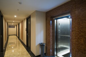 Pasillo de hotel con suelo de mármol, un cesto de basura y un ascensor.