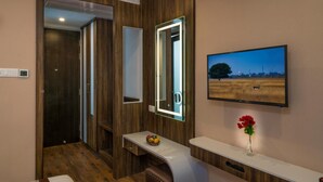 A modern bathroom with a wooden panel design, a mirror with integrated lighting, a television mounted on the wall, and a small table with a fruit bowl and a vase.