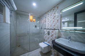 A modern bathroom with a glass shower enclosure, a white sink, and a mirror with integrated lighting. - Hotel CR Grande (Madurai)