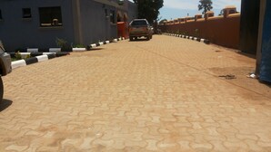 A paved driveway leading to a building with a blue exterior and a vehicle parked in the distance. - Skypa Hotel (Yumbe)