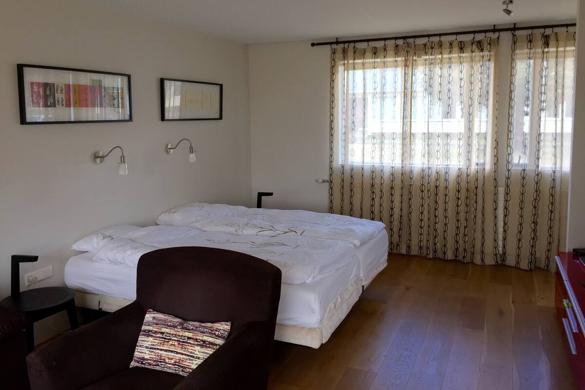 A bedroom with a bed, a chair, a desk, and a window with curtains.