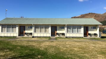 A two-story motel with a green roof, multiple windows, and a grassy lawn in front.