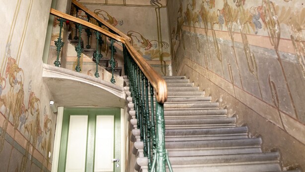 Una escalera con diseños florales ornamentales en el techo y barandales verdes.