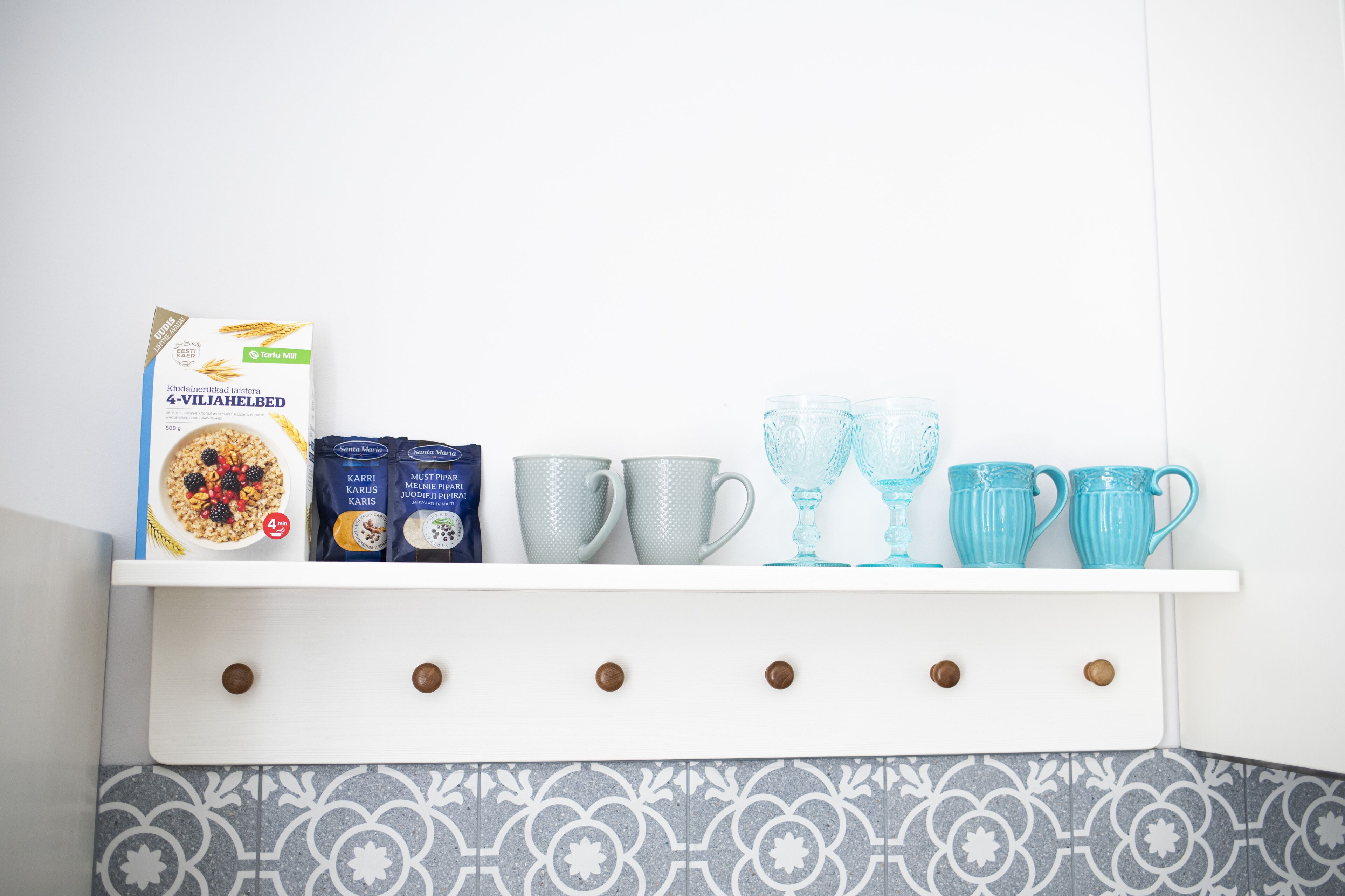 A kitchen shelf with a cereal box, two packets of coffee, and four blue cups.