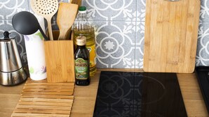 Una encimera de cocina con tabla de cortar, espátulas de madera, una botella de aceite de oliva, una cafetera y una plancha eléctrica negra.