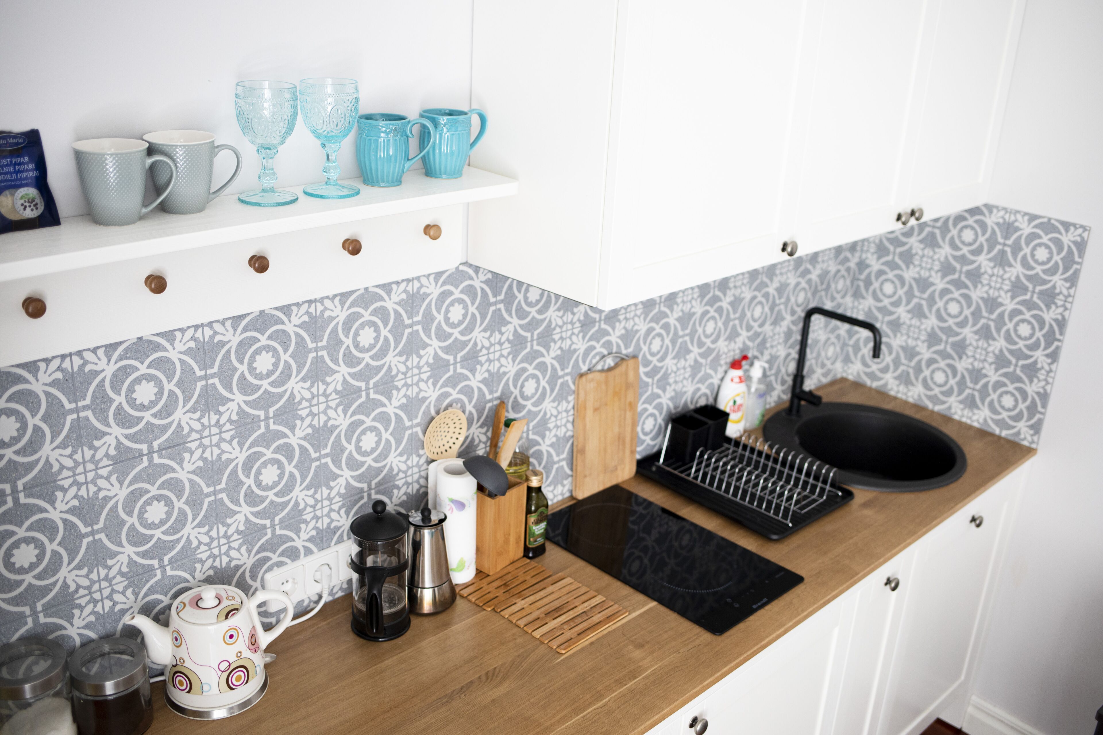 A kitchen with a wooden countertop, a black sink, and a patterned backsplash.