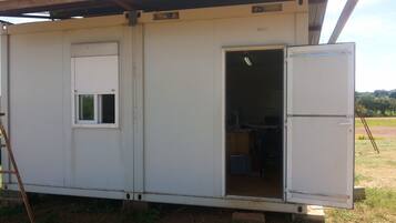 A mobile home with a single door open, revealing a kitchen area with a refrigerator and a window.