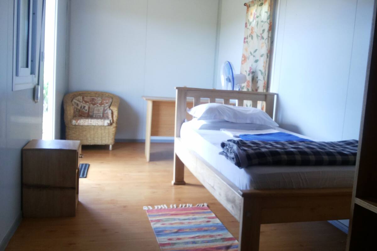 Un dormitorio con cama de madera, una silla, una mesita y un tapete colorido.