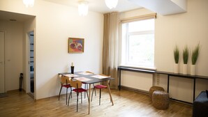 A dining area with a table and chairs, a radiator, a window with curtains, and a potted plant on a shelf. - City heart Kvartal-Tartu Home Apartments (Tartu)