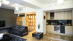 A modern living room with a black sofa, a coffee table, and a TV. Adjacent is a kitchen with wooden cabinets and a microwave. - City heart Kvartal-Tartu Home Apartments (Tartu)