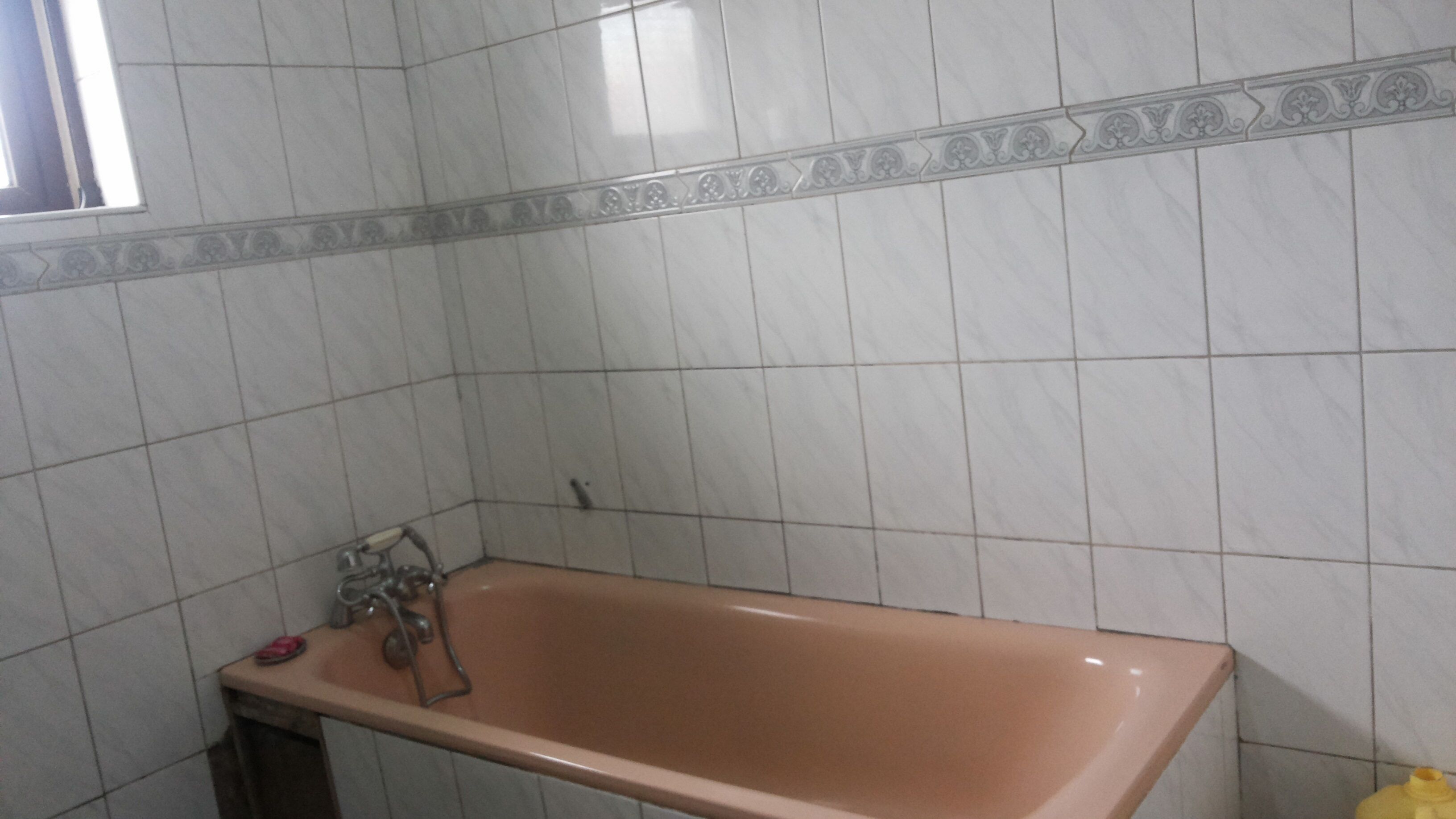 A bathroom with a bathtub, a sink with a faucet, and a toilet. The walls are tiled with a decorative border.