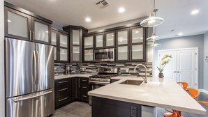 A modern kitchen with stainless steel appliances, dark cabinetry, and a central island with bar stools. - Exclusive Retreats White Rim 3371 - 3 Bedroom 3.5 bath, Private Hot Tub (Moab)