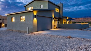 A modern two-story house with a flat roof, large windows, and a gravel driveway. - Exclusive Retreats White Rim 3371 - 3 Bedroom 3.5 bath, Private Hot Tub (Moab)