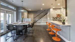A modern kitchen with a central island, a dining area with a marble table, and a staircase leading to an upper level. - Exclusive Retreats White Rim 3371 - 3 Bedroom 3.5 bath, Private Hot Tub (Moab)
