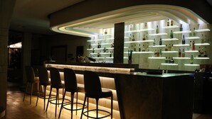 Een bar met een modern design, met een gebogen toonbank en meerdere verlichte planken waarop flessen staan. Vier barkrukken zijn er voor de toonbank gezet.
