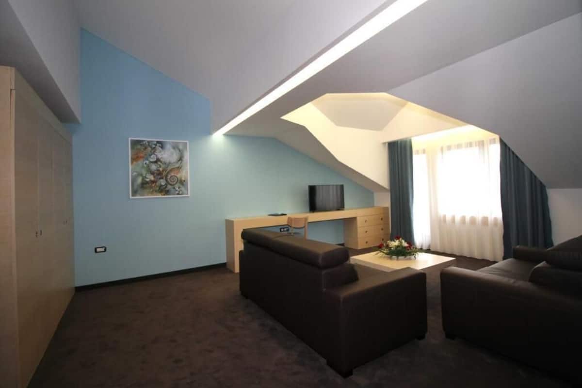 A modern living room with a loft-style ceiling, a flat-screen TV, a sofa, a coffee table, and a painting on the wall.