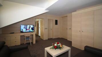 A room with a TV, a desk, a chair, a sofa, a table with flowers, and wooden wardrobes.