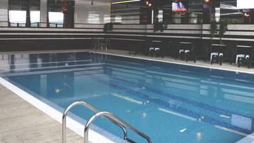 Une piscine intérieure avec des lignes de démarcation bien visibles, un escalier en métal et des chaises longues disposées le long du bord de la piscine.