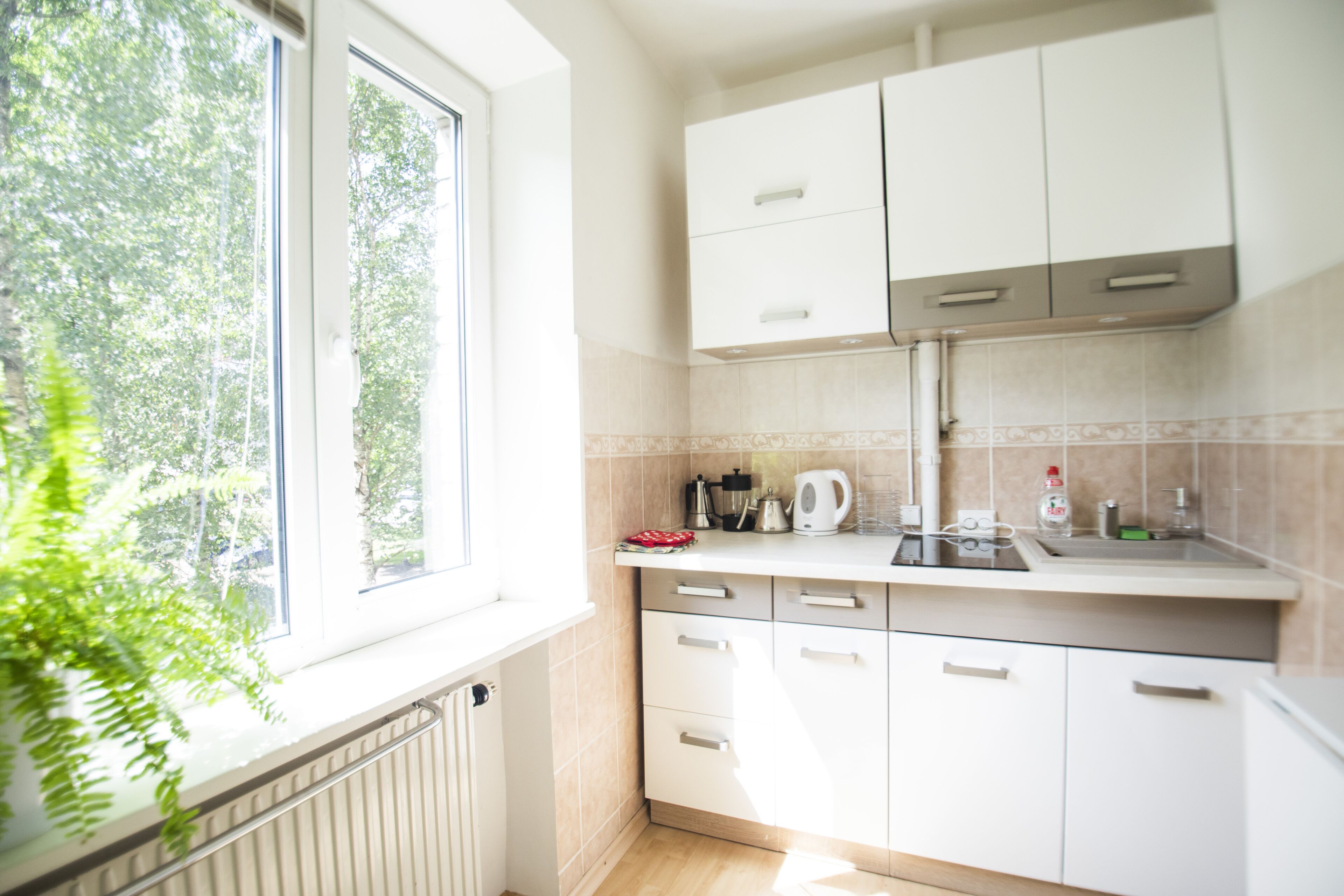 A modern kitchen with white cabinets, a window, and a radiator.