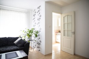A living room with a sofa, a coffee table, a potted plant, and a door leading to a kitchen. - Aura City Center Tartu Holidays (Tartu)