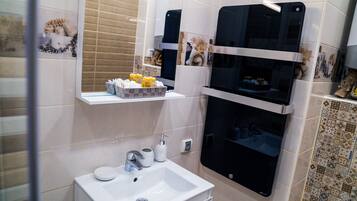 Un baño con lavamanos blanco, un espejo y repisas con artículos de aseo.