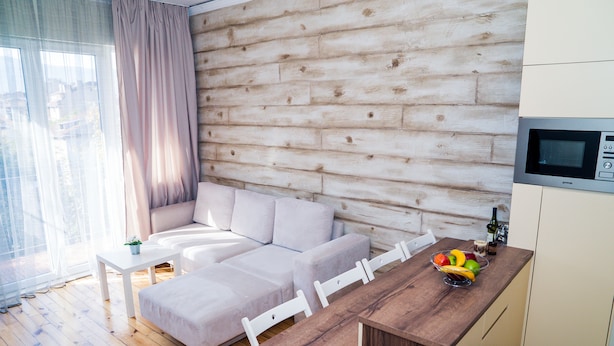Un espace de vie moderne avec un mur en bois, un canapé, une table à manger avec des chaises et un coin cuisine équipé d’un four à micro-ondes.