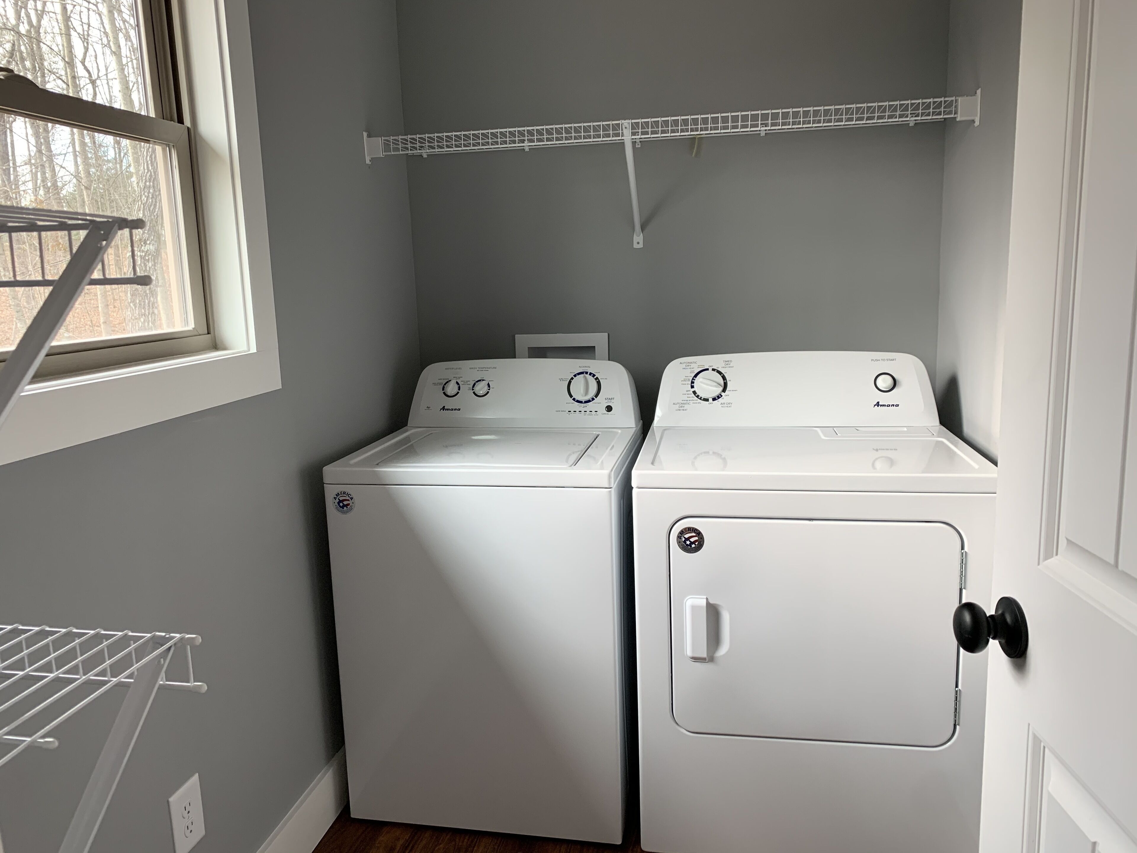 Une buanderie équipée de deux machines à laver et de deux sèche-linge à chargement frontal, tous deux de couleur blanche, d’un étendoir et d’une fenêtre donnant sur les arbres.