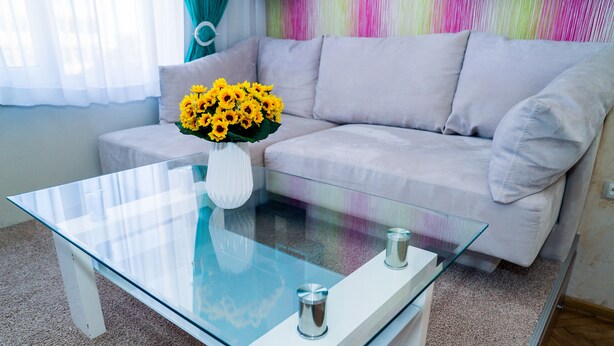 Ein modernes Wohnzimmer mit einem Glastisch, einem weißen Sofa und einer Vase mit gelben Blumen.