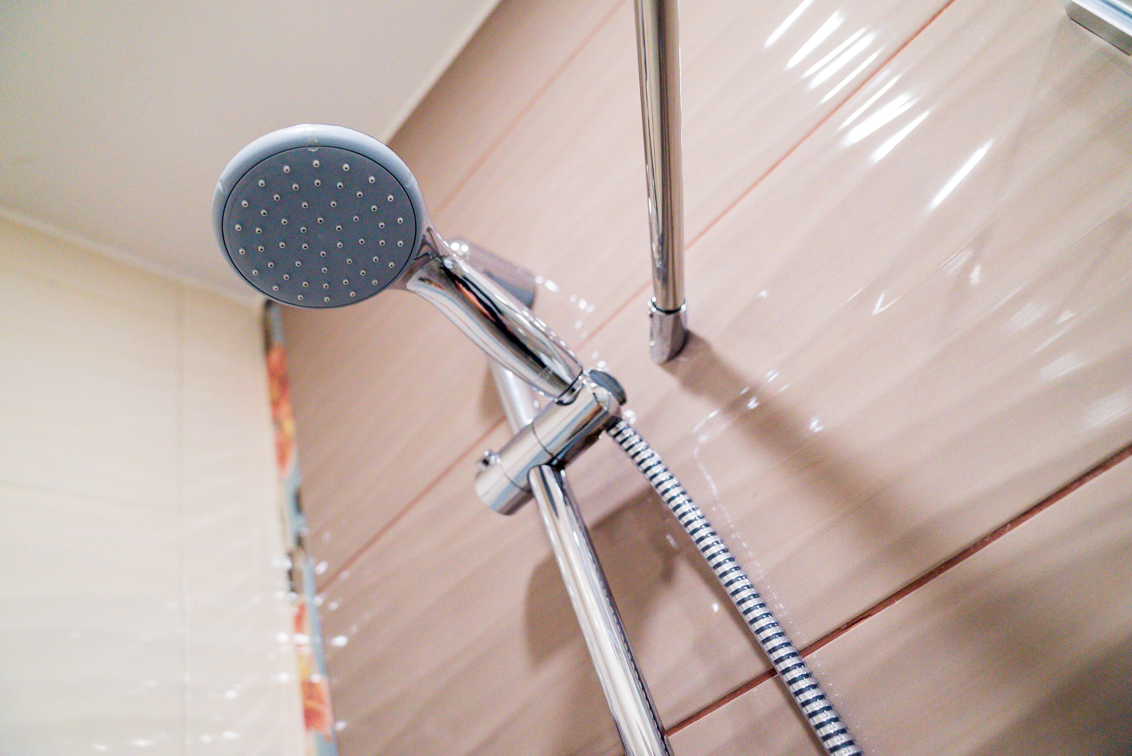 Un cabezal de ducha con manguera flexible, fijado a una pared con azulejos.