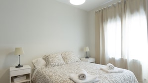 Un dormitorio con una cama, dos mesitas de noche, una lámpara sobre cada una y una ventana con cortinas.