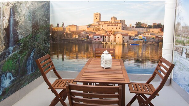 Un conjunto de mesa y sillas de madera frente a un mural que muestra un pueblo histórico a orillas de un río.