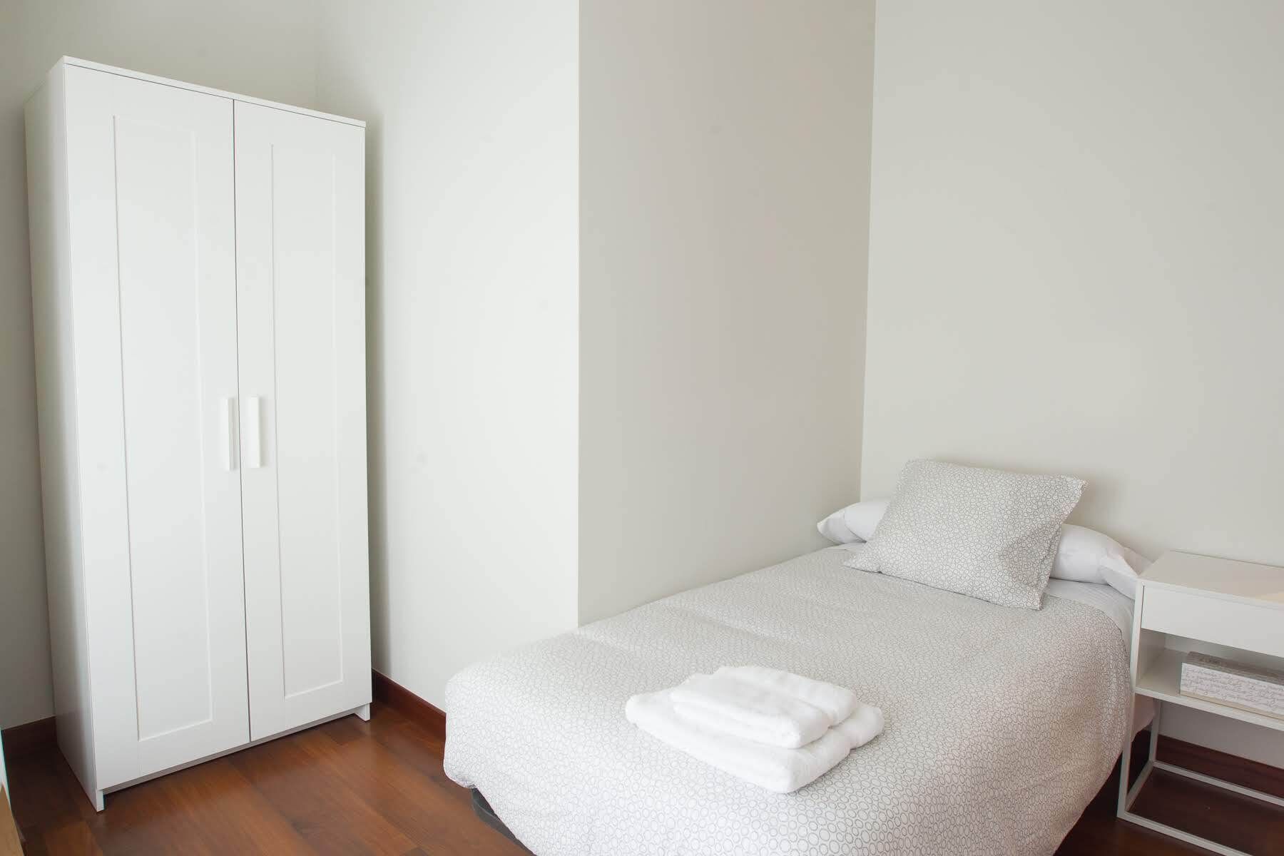 A bedroom with a bed, a white wardrobe, and a bedside table.