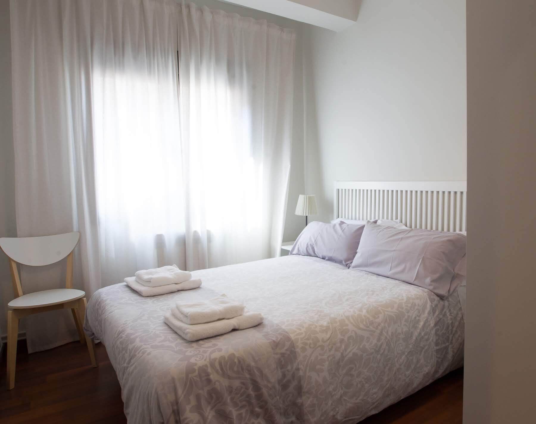Una cama bien tendida con un edredón estampado, una lámpara de noche y una silla con toallas dobladas.
