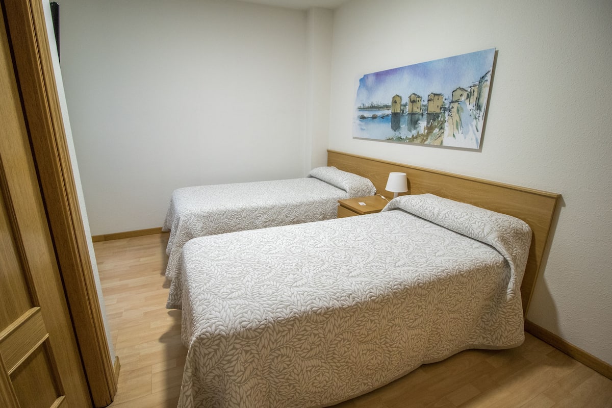 Habitación de hotel con dos camas, cabecero de madera, un cuadro en la pared y suelo de madera.