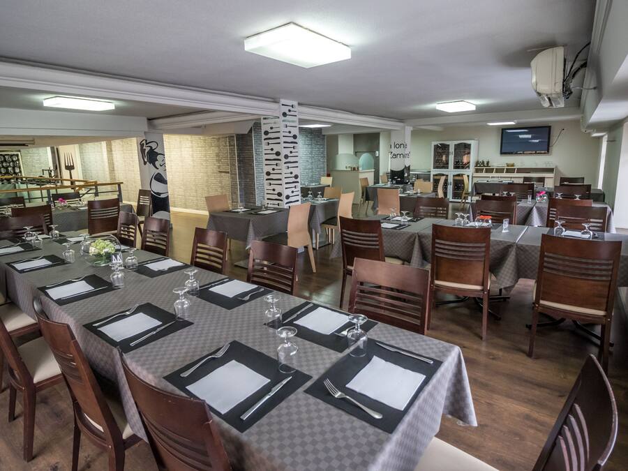 Un comedor con mesas dispuestas para el servicio, sillas de madera y una cocina al fondo.