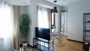 Una sala de estar moderna con un televisor de pantalla plana, una planta en maceta y una mesa de centro de vidrio.