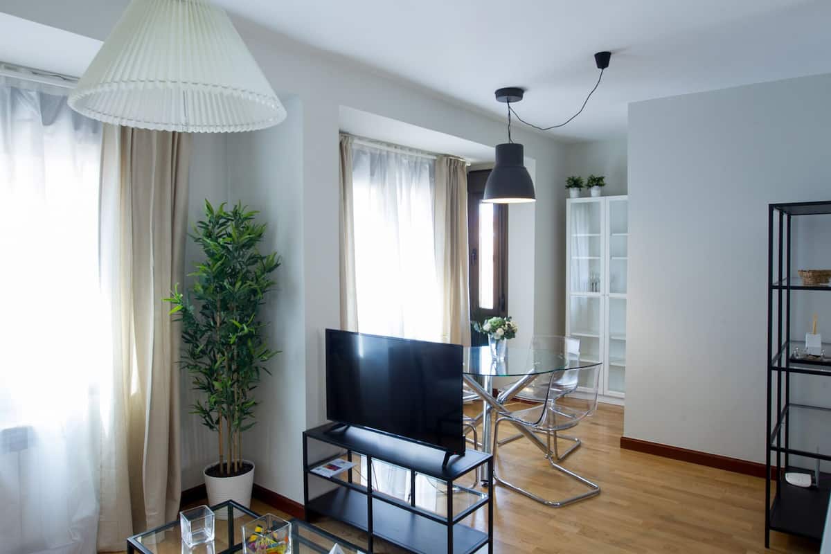 Una sala de estar moderna con un televisor de pantalla plana, una planta en maceta y una mesa de centro de vidrio.