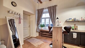A cozy room with a wooden floor, a desk with a chair, a mirror, a clock, and a window with curtains.