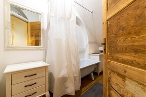 Un baño con puerta de madera, tocador blanco con cajones, espejo y cortina de ducha.