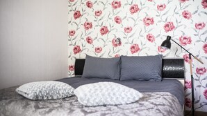 A bedroom with a bed, pillows, a lamp, and floral wallpaper. - Tiigi Bibliotheca- Tartu Home Apartments (Tartu)