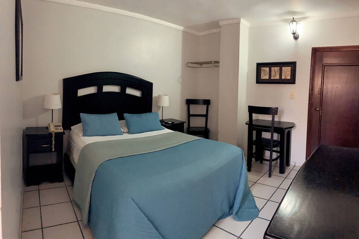 A bedroom with a bed, bedside tables, a chair, a desk, and a door.