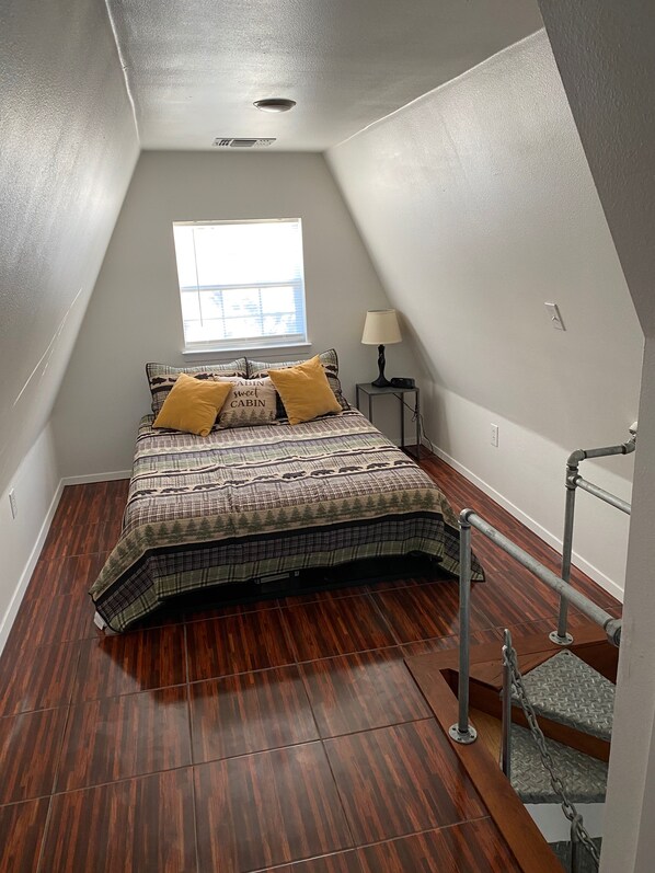 A bedroom with a bed, a window, a lamp, and a staircase.