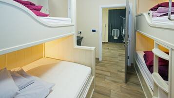 A hotel room with bunk beds, a bathroom with a shower, and a wooden floor.
