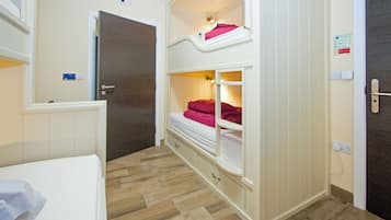 Habitación con literas, piso de madera, puerta blanca y una mesita de noche pequeña.