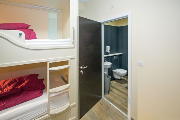 A bunk bed with red bedding, a white sink, and a toilet in a bathroom.