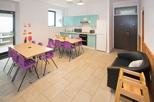 Una cocina moderna con armarios verde azulado, un comedor con sillas moradas y un sofá negro con una escalera de madera.