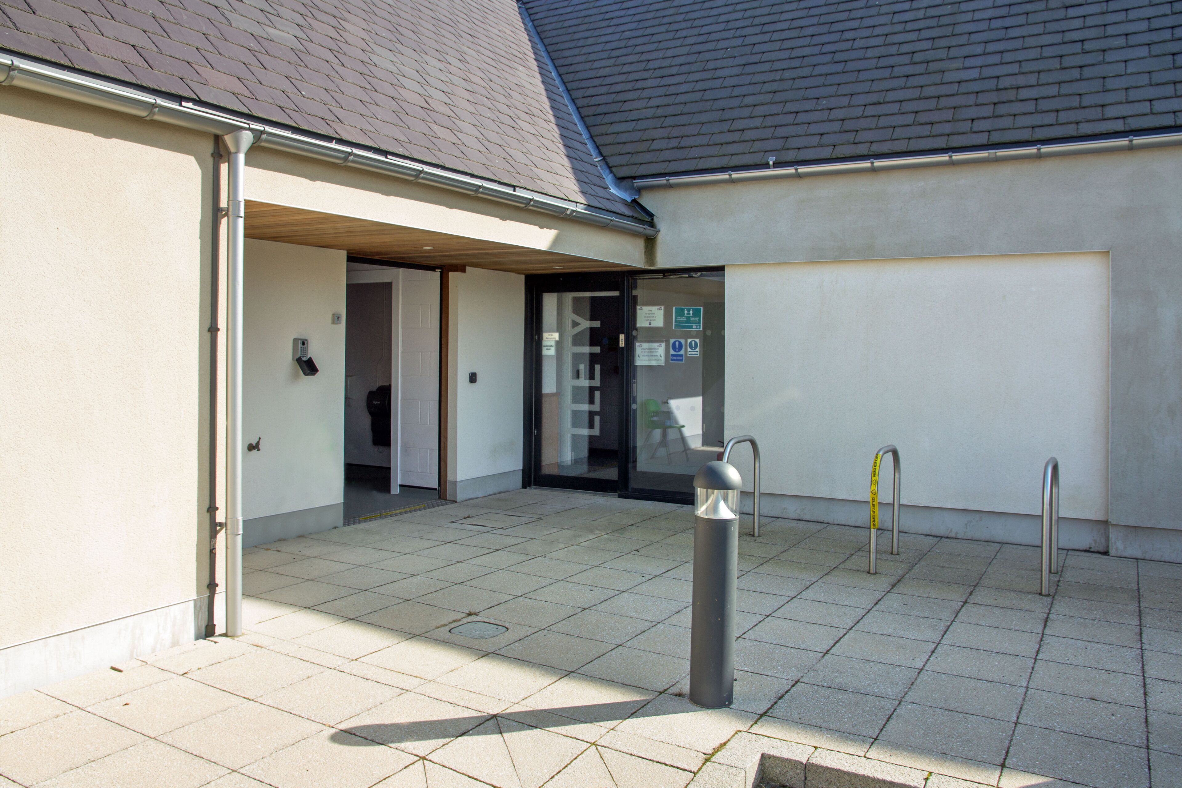 A building entrance with a tiled pavement, a door, and a small outdoor seating area.