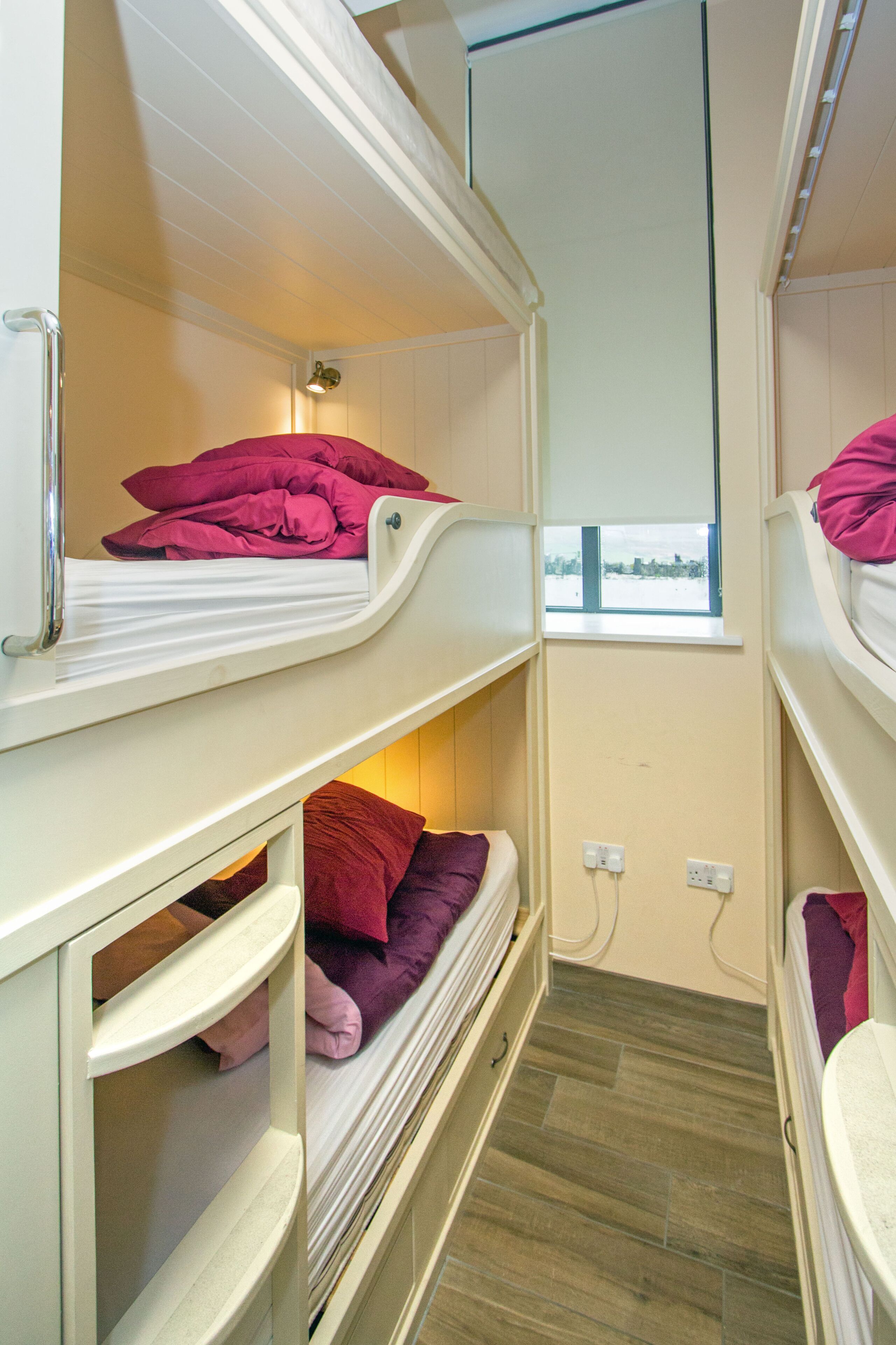A narrow room with bunk beds, a window, and a power outlet.