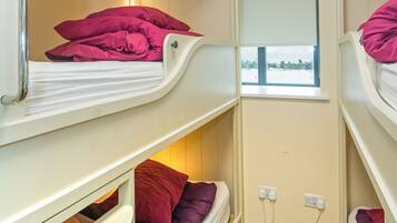 A narrow room with bunk beds, a window, and a power outlet.