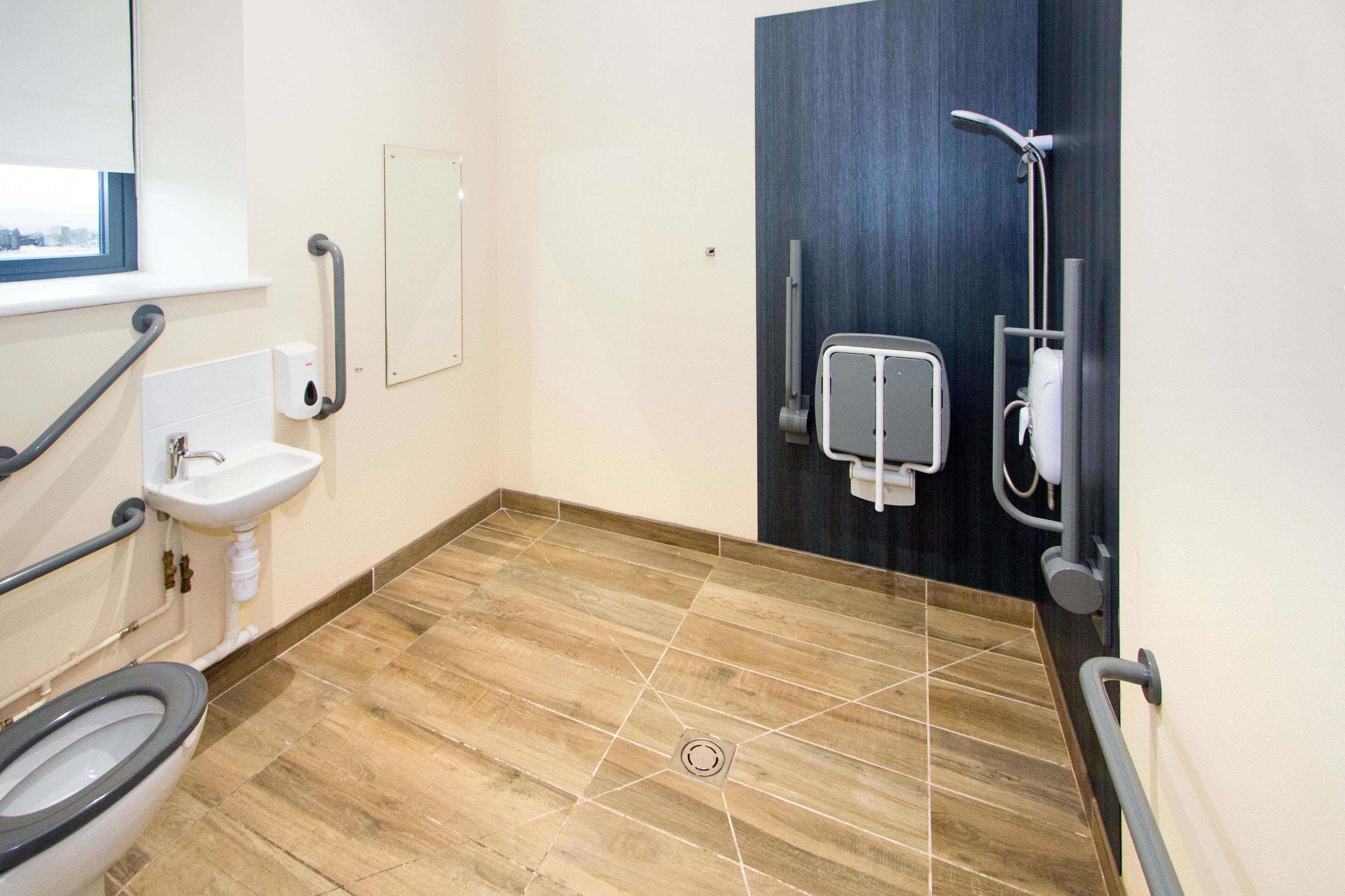A modern bathroom with a wooden floor, a sink, a toilet, and a shower area.